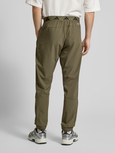 Männermodel trägt Regular Fit Sweatpants mit elastischem Bund mit Logo-Print Modell 'TECH APP S-PANT' von adidas Training, Optik: Unifarben, Label-Print, Logo-Detail, Kontrast-Nähte, Batist, Ganzkörperansicht Rückansicht.
