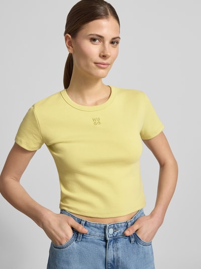 Frauenmodel trägt Slim Fit T-Shirt aus Baumwoll-Mix Modell 'DELANOR' von HUGO in Optik: Unifarben mit Logo-Stitching und Rundhals-Ausschnitt, Ärmelform: Kurzarm, Materialverarbeitung: Stretch, Länge: Cropped, Nahaufnahme Oberkörper.