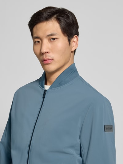 Mannelijk model draagt Regular Fit Bomberjacke mit Stehkragen van Guess in blauw, elastische boorden, zijzakken, ritssluiting, Nahaufnahme bovenlichaam.