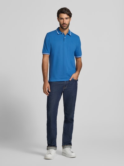 Męski model nosi Slim Fit Poloshirt mit Label-Stitching od bugatti w kolorze niebieskim, czysta bawełna, kołnierzyk polo, zapięcie na guziki, długość tyłu w rozmiarze M: 67 cm, krój slim fit, widok całej sylwetki z przodu.