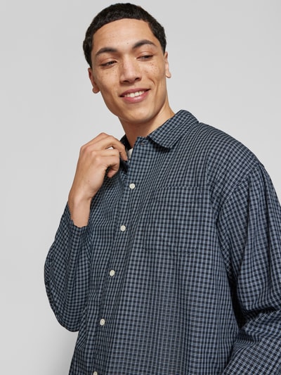Mannenmodel draagt Regular Fit Freizeithemd aus Baumwolle Modell 'AUSTIN' van Jack & Jones, donkerblauw ruitpatroon, borstzak, kentkraag, knoopsluiting, katoen, relaxed silhouet, schouderbreedte 45 cm, mouwlengte 57 cm, ruglengte 60 cm, Nahaufnahme bovenlichaam.