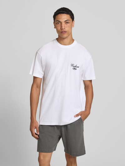 Männermodel trägt weißes T-Shirt mit Logo-Stitching Modell 'Gracious' von Carhartt Work In Progress, Rundhalsausschnitt, Ganzkörperansicht von vorne.