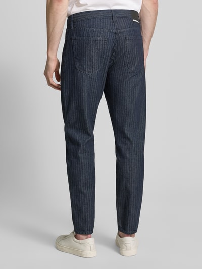 Männermodel trägt Tapered-Fit Herren Jeans aus reiner Bio-Baumwolle von Armedangels Modell 'HERRINGBONE' in Denim-Optik, Label-Patch, 5-Pocket-Design, Mid Waist, Ganzkörperansicht Rückansicht.