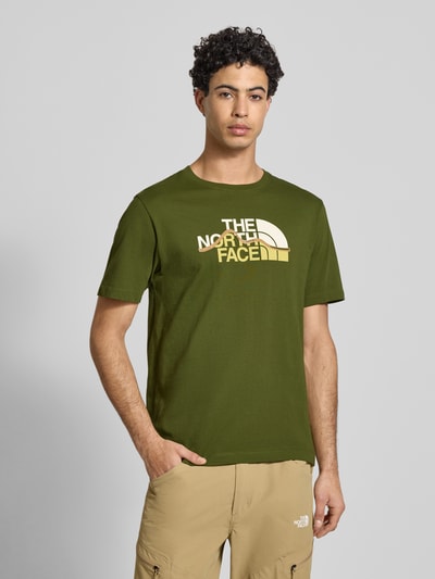 Männermodel trägt Regular Fit T-Shirt aus reiner Baumwolle Modell 'MOUNTAIN LINE' von The North Face in Olive mit Label-Print, Nahaufnahme Oberkörper. Herren T-Shirt, Rundhalsausschnitt, Rückenlänge bei Größe M 70 cm.