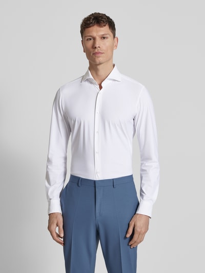 Männermodel trägt Slim Fit Business-Hemd mit Kentkragen von JOOP! Collection in Weiß, glatter Stoff, lange Ärmel, Ganzkörperansicht von vorne.
