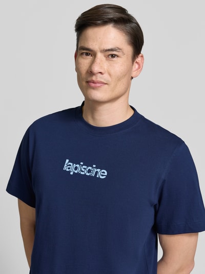 Männermodel trägt Regular Fit T-Shirt aus reiner Baumwolle Modell 'HASPEN' von SELECTED HOMME in Optik: Unifarben mit Schriftzug-Applikation, Rundhals-Ausschnitt und Kurzarm, Material reine Baumwolle, Nahaufnahme Oberkörper.