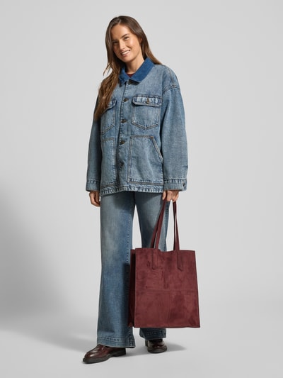 Kobiece model nosi Tote Bag mit Label-Detail Modell 'AMY' od LIEBESKIND BERLIN w kolorze bordowym, prostokątny kształt, matowa tekstura, główna przegroda z zapięciem na zatrzask, uchwyty, przegródka wewnętrzna z zamkiem błyskawicznym, szerokość 35 cm, długość 40 cm, głębokość 11 cm, długość paska na ramię 60 cm, widok całej sylwetki z przodu.