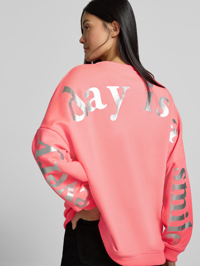 Männermodel trägt Oversized Sweatshirt aus Baumwoll-Mix Modell 'Everyday' von miss goodlife in leuchtendem Rosa mit Statement-Print und Strasssteinbesatz, gerippte Abschlüsse, Ganzkörperansicht Rückansicht.