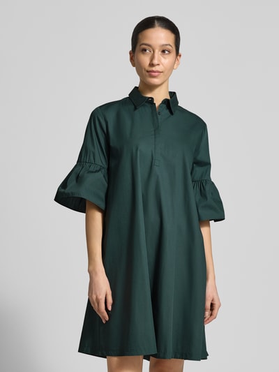 Frauenmodel trägt knielanges Hemdblusenkleid mit Kentkragen Modell 'EPOCHE' von EMME aus reiner Baumwolle, lockerer Schnitt, Volants, Ganzkörperansicht von vorne.