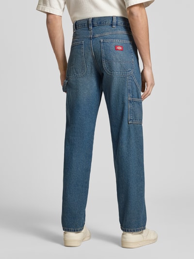 Męski model nosi Regular Tapered Fit Jeans im Used-Look od Dickies, niebieski dżins, krój tapered fit, bawełna, widoczne kieszenie, szerokość w rozmiarze 32/32: 40 cm, długość nogawki od wewnątrz: 80 cm, widok całej sylwetki od tyłu.