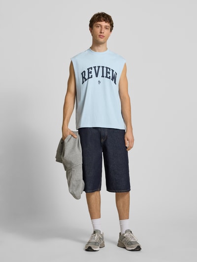 Männermodel trägt Tanktop mit Logo-Print von REVIEW in Hellblau, Reine Baumwolle, Gerader-Schnitt, Rundhalsausschnitt, Rückenlänge 68 cm, Ganzkörperansicht von vorne.