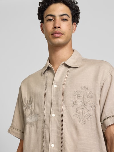 Männermodel trägt Relaxed Fit Freizeithemd aus Lyocell-Mix Modell 'Menton' von Jack & Jones, beige, florales Stitching, Kurzärmelig, Nahaufnahme Oberkörper. Rückenlänge 72 cm, Schulterbreite 52 cm, Ärmellänge 25 cm. Baumwolll-Lyocell-Mix, Kentkragen, Knopfleiste.