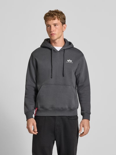 Męski model nosi Hoodie mit Label-Details od Alpha Industries, mieszanka bawełny, luźny krój, kieszeń kangurka, prążkowane wykończenia, Długość tyłu w rozmiarze M: 69 cm, Długość rękawów w rozmiarze M: 70 cm, kolor ciemnoszary, matowa tekstura, Ganzkörperansicht z przodu.