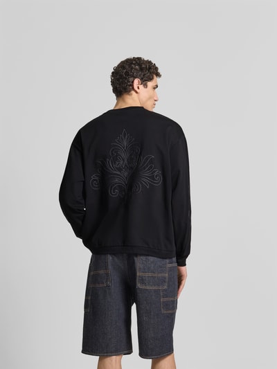 Männermodel trägt Oversized Sweatshirt aus Baumwolle von Don't Waste Culture in Schwarz mit florale Stickereien, Rückenlänge 66 cm, Ganzkörperansicht Rückansicht.