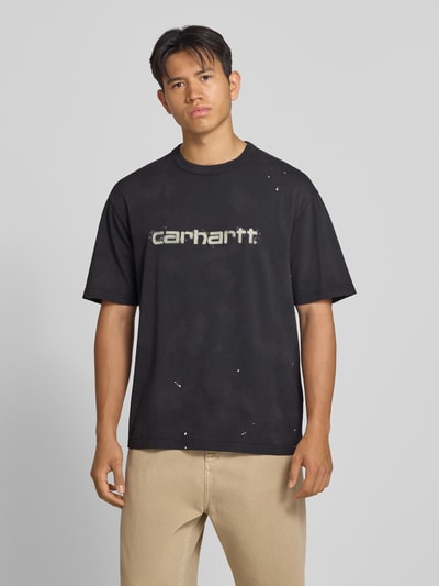 Męski model nosi t-shirt Regular Fit T-Shirt aus reiner Baumwolle Model 'Painter' von Carhartt Work In Progress, czarny z nadrukiem, detal z logo, Długość tyłu w rozmiarze M: 72 cm, Ganzkörperansicht von vorne.