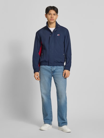 Mannenmodel draagt Regular Fit blouson met logo-stitching van Tommy Hilfiger in effen kleuren, satijn materiaalverwerking, lange mouw, opstaande kraag, drukknoopsluiting met ritssluiting, logo-applicatie, steekzakken met drukknoop, elastische rompzoom en mouwboord, look: effen, ganzekörpervooraanzicht.