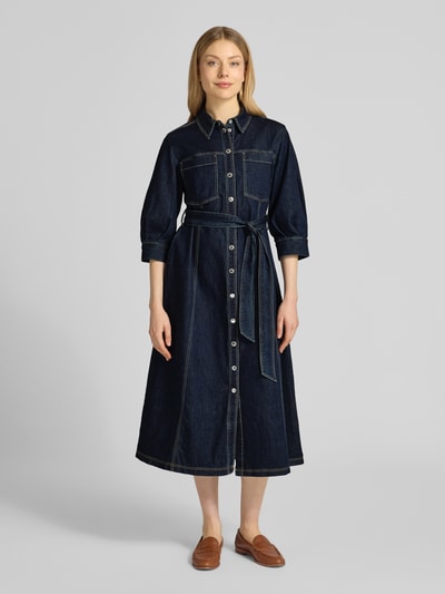 Kobiece model prezentuje sukienka koszulowa z mieszanki bawełny i lyocellu o linii a w imitacji denimu z kołnierzykiem koszulowym, listwą guzikową i wiązanym paskiem, długość tyłu w rozmiarze 36: 121 cm, szerokość w rozmiarze 36: 51 cm, długość rękawów w rozmiarze 36: 43 cm, Hemdblusenkleid mit Bindegürtel od Betty Barclay, widok całej sylwetki z przodu.