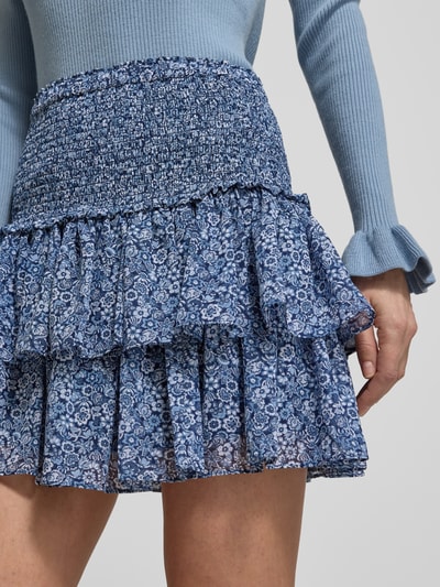 Vrouwenmodel draagt Minirok met Volantsaum en Smok-Details van MICHAEL Michael Kors, A-lijn, elastische taille, bloemenpatroon, ondoorzichtige onderrok, close-up voorkant.