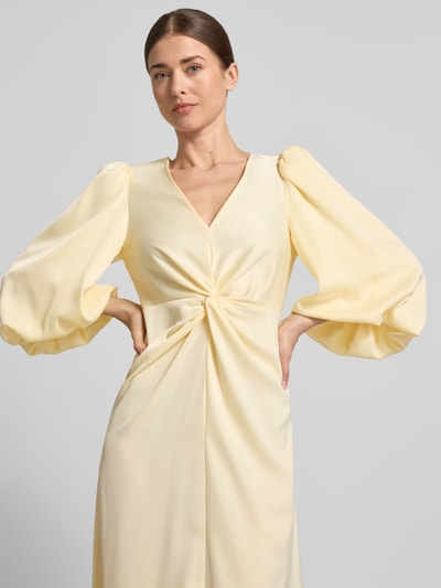Frauenmodel trägt Maxikleid mit Ballonärmeln Modell 'THEA' von YAS in hellem Gelb, Material-Mix mit Stretch-Anteil, taillierter Schnitt, V-Ausschnitt und Knoten-Detail, glatte Textur, Nahaufnahme Oberkörper.