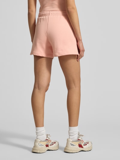 Modelka nosi Regular Fit Sweatshorts aus reiner Baumwolle od Lacoste, efekt: jednolity kolor, krój regular fit, wyhaftowane logo, tunel, ściągacz: elastyczny, wpuszczane kieszenie, bawełna; pełny widok sylwetki od tyłu.