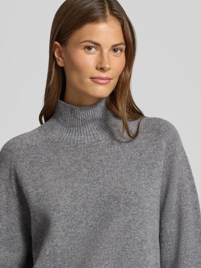 Frauenmodel trägt Strickpullover mit Stehkragen Modell 'LYZIMA' von DRYKORN aus reiner Baumwolle in Grau, Nahaufnahme Oberkörper.
