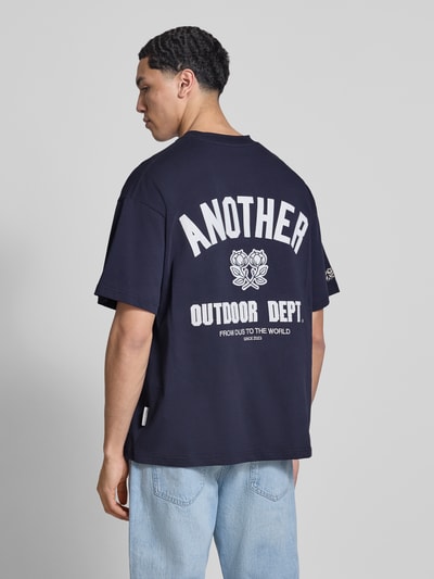 Männermodel trägt Regular Fit T-Shirt mit Logo-Print von ANOTHER COTTON LAB, dunkelblau, weiße Schrift, reine Baumwolle, Ganzkörperansicht Rückansicht.