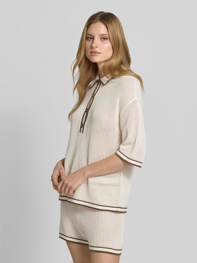 Frauenmodel trägt Strickshirt mit Polokragen und Knopfleiste von Style Icon Collection aus reiner Baumwolle, grob gestrickt, cremefarben mit braunen Details, gerader Schnitt, überschnittene Schultern, 3/4-Arm, Ganzkörperansicht von vorne.