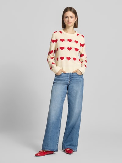 Frauenmodel trägt Regular Fit Pullover mit Allover-Muster Modell 'ELYNA' von Only in Creme mit roten Herzen, Strick, Rundhals, langarm, Ganzkörperansicht von vorne.