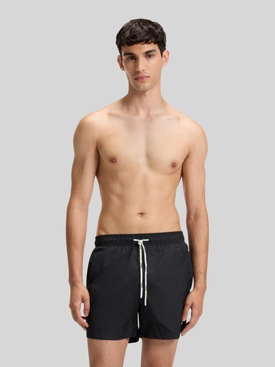 Männermodel trägt Badeshorts mit Label Print Modell 'HAITI' von HUGO, unifarben, elastischer Bund, Ganzkörperansicht von vorne.