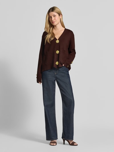 Vrouwenmodel draagt Strickjacke aus Viskose-Mix mit V-Ausschnitt van Apricot, donkerbruin, losse regular fit, lichte textuur, opgestikte zakken, grote knopen, rechte blauwe jeans, volledige lichaamsweergave van voren.