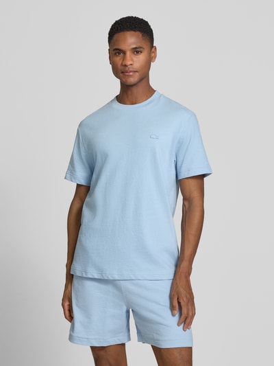 Męski model nosi Regular Fit T-Shirt aus reiner Baumwolle von Lacoste, gładki jasnoniebieski, krój regular fit, okrągły dekolt, krótki rękaw, label patch, delikatny dżersej z czystej bawełny, całopostaciowy widok z przodu.