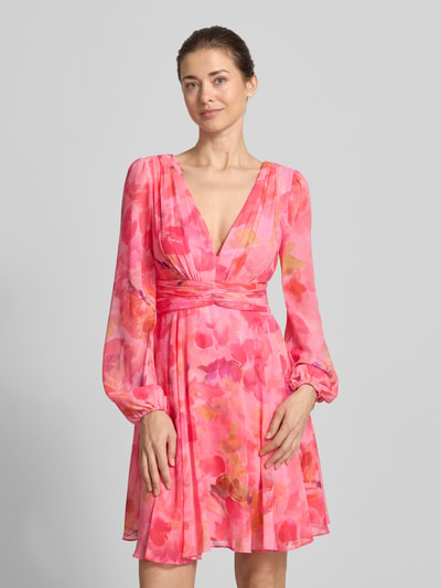 Frauenmodel trägt Cocktailkleid mit Ballonärmeln und V-Ausschnitt von Jake*s Cocktail aus Chiffon mit tailliertem Schnitt, Minikleid mit V-Ausschnitt und Ballonärmeln, rückseitigem V-Ausschnitt und Rückenreißverschluss in Pink mit floralem Muster, Rückenlänge 91 cm, Brustweite 40 cm, Ärmellänge 65 cm, Ganzkörperansicht von vorne.