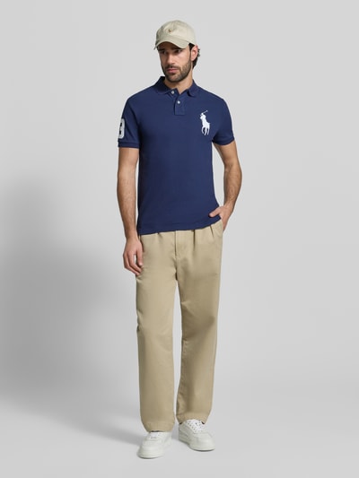 Männermodel trägt Shaped Fit Poloshirt aus reiner Baumwolle von Polo Ralph Lauren, uni dunkelblau, Polokragen, Piqué, Kurzarm, Ganzkörperansicht von vorne.