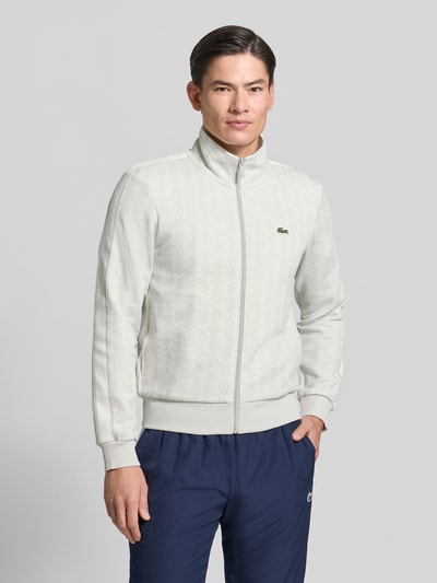 Männermodel trägt Regular Fit Sweatjacke mit Reißverschluss von Lacoste in Hellgrau mit feiner Textur, Ganzkörperansicht von vorne. Herren Sweatjacke von Lacoste