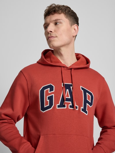 Mannelijk model draagt Hoodie mit Kängurutasche van GAP in een los vallende fit, katoenmix, rood met label-stitching, capuchon en kangoeroezak, ribboorden, detailopname bovenlichaam.