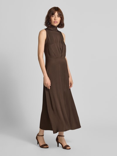 Frauenmodel trägt Maxikleid mit Stehkragen und Drapierungen Modell 'AMABEL' von DRYKORN, brauner Material-Mix, A-Linie, Ganzkörperansicht von vorne.