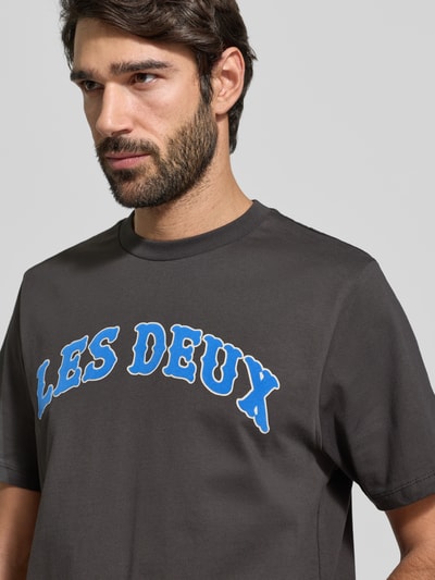 Męski model nosi T-Shirt z label-print 'Brady' od Les Deux, szary kolor, czysta bawełna, regular fit, zbliżenie na górną część ciała.