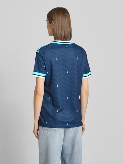 Modelka nosi DFB Auswärtstrikot 2026 od adidas Sportswear, wielokolorowe, krój regular fit, z logo DFB i naszywką, dekolt w serek, krótki rękaw, widok całej sylwetki od tyłu.