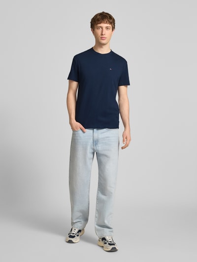 Männermodel trägt Regular Fit T-Shirt aus reiner Baumwolle von Tommy Jeans, unifarben, Logo-Stitching, Jersey, Ganzkörperansicht von vorne.