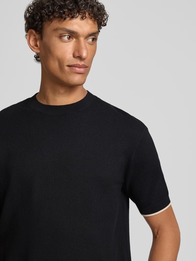 Männermodel trägt Strickshirt mit Strukturmuster und Rundhalsausschnitt von Emporio Armani, schwarze Baumwolle, Nahaufnahme Oberkörper.