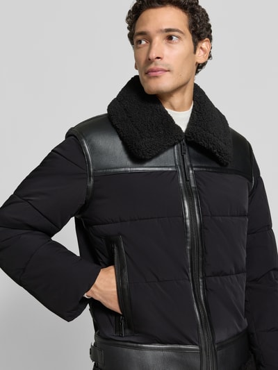 Männermodel trägt Steppjacke mit Zweiwege-Reißverschluss Modell 'FLINT' von khujo in Schwarz mit Teddyfellkragen, Nahaufnahme Oberkörper.