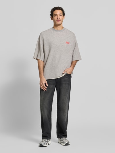 Männermodel trägt Oversized T-Shirt aus Baumwoll-Mix von American Vintage in Grau mit Logo-Print, elastisches Material, Ganzkörperansicht von vorne.