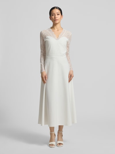 Frauenmodel trägt Tailliertes Brautkleid mit V-Ausschnitt Modell 'Joanna' von GUIDO MARIA KRETSCHMER WOMAN aus Elastischer-Material-Mix, Langärmelig, Oberteil aus Spitze, blickdichter Rockteil, Nahtreißverschluss, Hochzeitsmode, Ganzkörperansicht von vorne.
