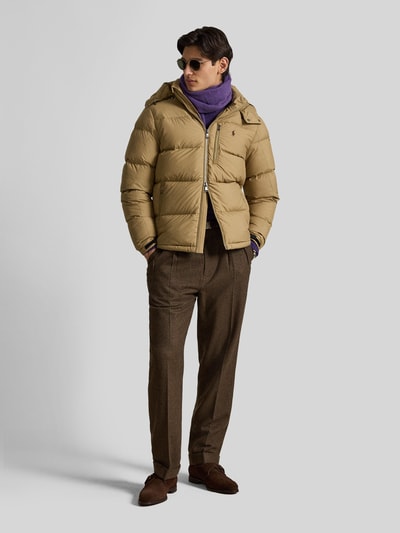 Männermodel trägt Regular Fit Daunenjacke mit Logo-Stitching von Polo Ralph Lauren in Beige, kombiniert mit brauner Hose, Ganzkörperansicht von vorne. Herren Daunenjacke von Polo Ralph Lauren
