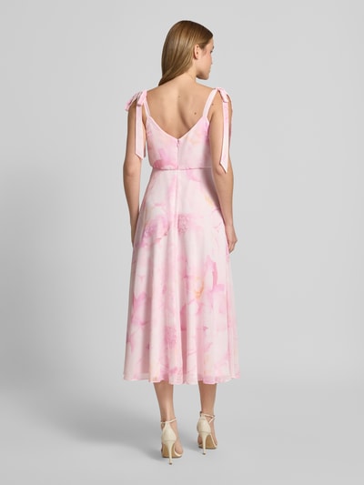 Frauenmodel trägt Knielanges Cocktailkleid mit floralem Allover-Print von Jake*s Cocktail in zartem Rosa, Zierschleifen, Taillierte Passform, blickdichter Unterrock, Ärmelloses-Design, Rückansicht Ganzkörperansicht.