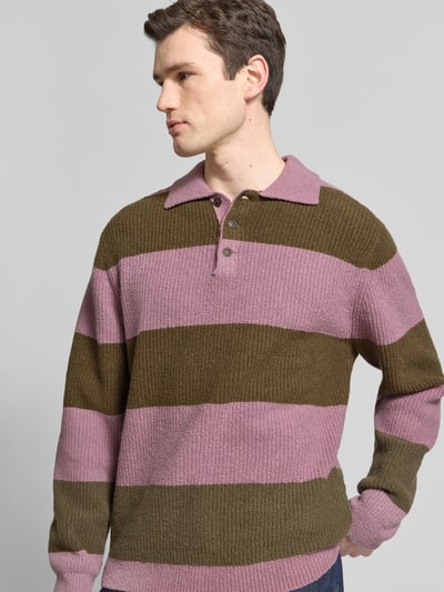 Männermodel trägt Strickpullover mit Polo-Kragen Modell 'Kimse' von Wood Wood in Rosa und Oliv, grob gestrickt, Nahaufnahme Oberkörper.