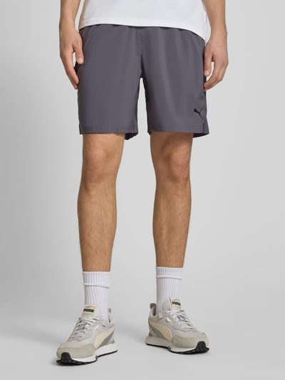 Männermodel trägt Shorts mit Logo und elastischem Bund von PUMA PERFORMANCE in Grau, Regular Fit, Ganzkörperansicht von vorne.
