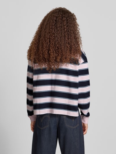 Frauenmodel trägt Cropped Poloshirt mit Label-Stitching von Guess Jeans aus reiner Baumwolle mit Knopfleiste und Longsleeve, Querstreifen in Rosa, Schwarz und Weiß, strukturierte Oberfläche, Ganzkörperansicht Rückansicht.