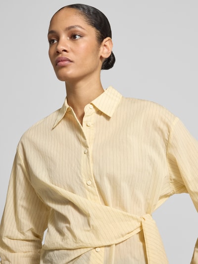 Frauenmodel trägt Regular Fit Bluse mit Knotendetail Modell 'CHIPITI' von Mango im Baumwoll-Mix, dezentes Hellgelb mit feinen Streifen, Nahaufnahme Oberkörper.