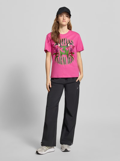 Vrouwenmodel draagt T-Shirt met Label-Print van adidas Sportswear in roze, katoen, regular fit, geribde ronde hals, vooraanzicht, ruglengte maat S 60 cm.